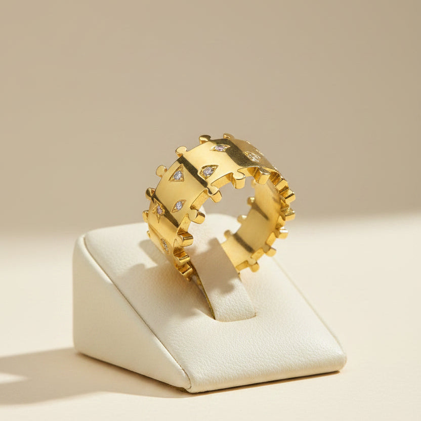 A wide gold ring with a crown-like textured design and small clear gemstones set into the sides, photographed on a clean white background.