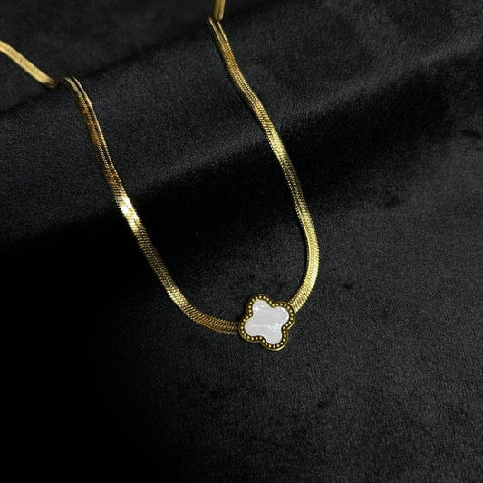 Gold necklace with a clover-shaped pendant on a black fabric background