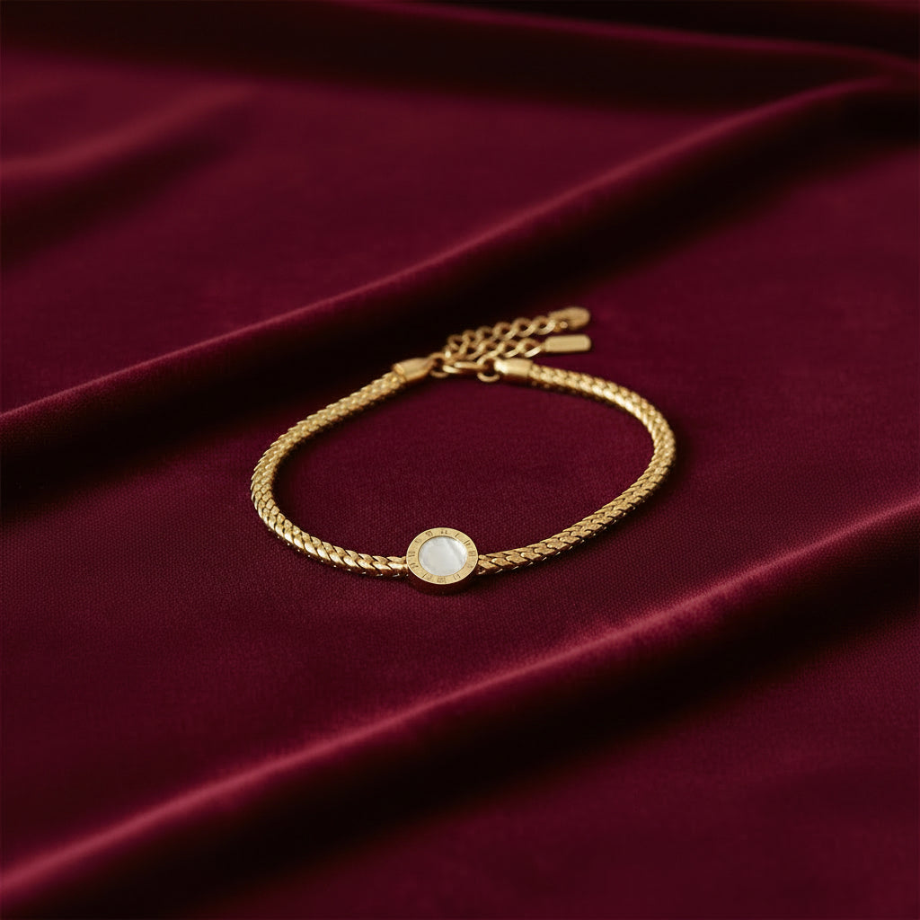 A gold-toned chain bracelet featuring a central round bezel-set white pearl with a textured gold border, displayed on a clean white background.
