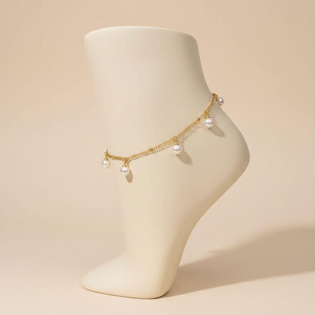A delicate gold chain anklet with three small white pearl charms, displayed on a black mannequin leg against a white background.