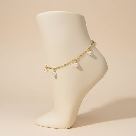 A delicate gold chain anklet with three small white pearl charms, displayed on a black mannequin leg against a white background.