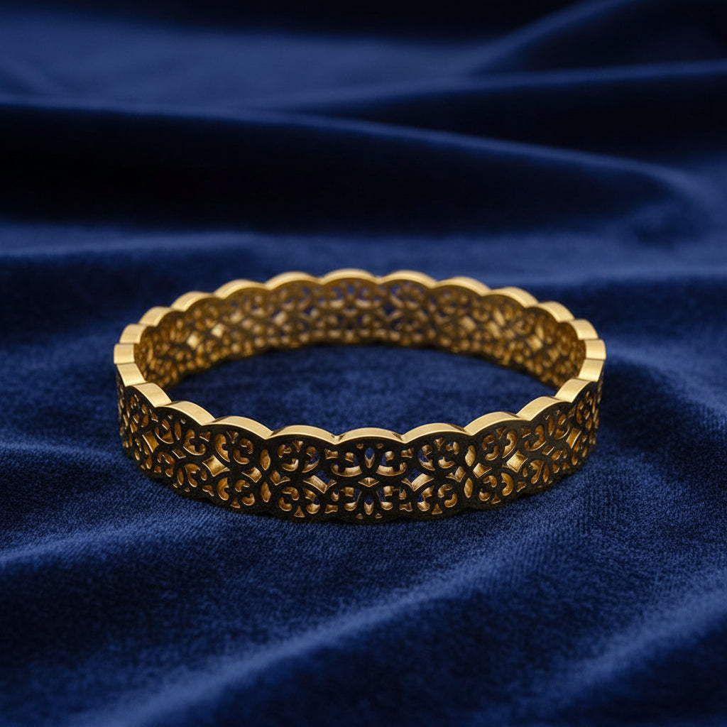A gold filigree bangle bracelet with an intricate openwork pattern and scalloped edges, displayed on a clean white background.